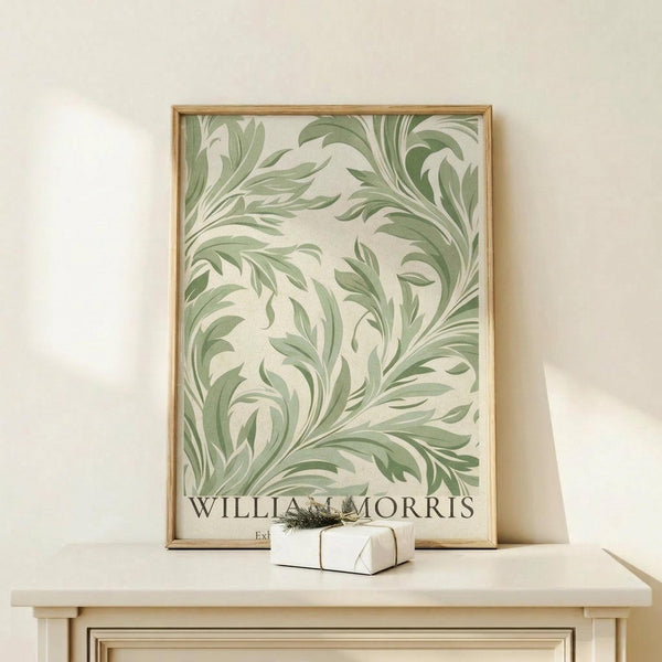 May include: Framed botanical art print with flowing green foliage pattern on cream background, displayed on light wood console table against white wall. Small white gift box with greenery sprig sits in front of the wooden-framed artwork. Soft natural lighting creates gentle shadows on the minimalist styled surface.