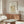 May include: Framed botanical poster with cream background and ornate green pattern featuring white and coral tulips, displayed on wooden sideboard in modern living room with white sculptural chair, glass coffee table, and minimalist decor in neutral tones