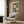 May include: Framed botanical art print with white and cream flowers, blue butterfly, and dark green foliage displayed on wood-paneled wall above beige upholstered armchair with geometric pillow, brass floor lamp and side table with open book nearby