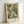 May include: Framed botanical art print featuring flowing green foliage in an ornate, swirling pattern against a cream background. The artwork displays elegant curved leaves and fronds in various shades of green, creating a decorative tapestry-like design. Text at bottom reads "WILLIAM MORRIS Exhibition Art - Floral Tapestry." Natural wood frame with white matting, positioned against a white wall with soft lighting casting gentle shadows.