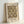 May include: Framed poster print featuring William Morris decorative pattern in earth tones of brown, cream, and gold. The intricate Victorian-style design shows repeating ornamental motifs with flowing organic shapes. Light wood frame displayed against white wall, leaning on surface, showing museum exhibition details and Morris's dates (1834-1896).