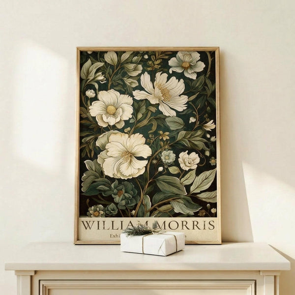 May include: Framed botanical poster with cream-colored flowers and dark green foliage on black background, displayed on light wood console table with small white gift box, against neutral wall in minimalist interior setting