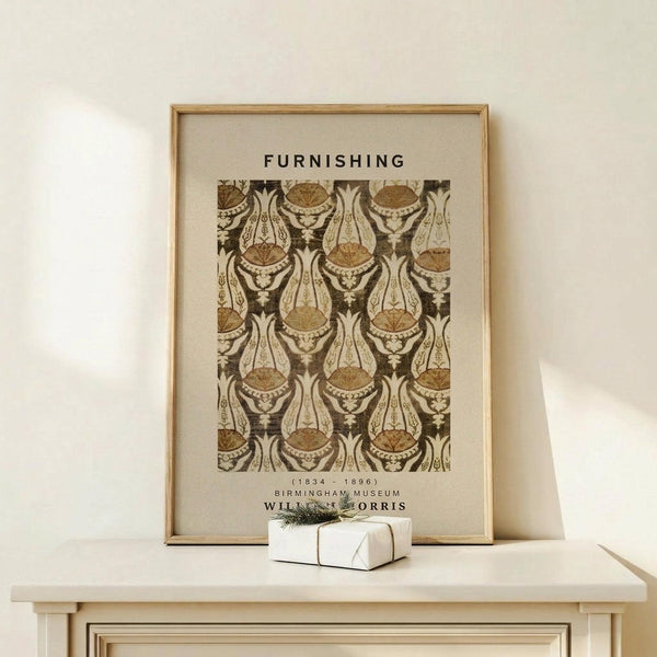 May include: Framed William Morris textile pattern print in brown and cream tones featuring ornate paisley and floral motifs, displayed on light wood furniture beside a small wrapped gift with greenery accent. The vintage-style poster has "FURNISHING" text above the decorative pattern and museum attribution below, set in a thin natural wood frame against cream wall.
