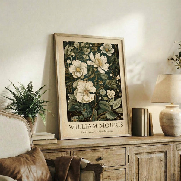 May include: Framed botanical poster with cream-colored mat displaying white and pale flowers with green foliage on dark background. Light wood frame sits on rustic wooden sideboard next to fern plant, books, ceramic vase and table lamp in warm neutral-toned living room setting.