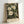 May include: Framed botanical art print featuring white and cream flowers with green foliage on dark background, displayed in light wood frame against white wall. Print shows "WILLIAM MORRIS" and "Exhibition Art - Serene Blossoms" text at bottom in vintage poster style.