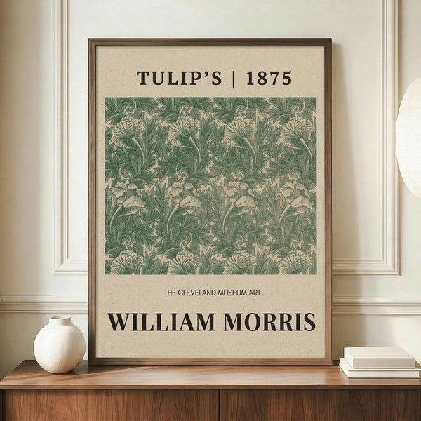 May include: Framed vintage botanical poster with green leafy tulip pattern on cream background, displayed on wooden sideboard next to white ceramic vase and stacked books against beige paneled wall in elegant room setting.