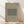 May include: Framed poster with beige background displaying "William Morris" and "COTTON" text above a green geometric pattern sample, labeled "EYE BRIGHT" below. Natural wood frame sits on light wooden floor against white wall with soft sunlight shadows.