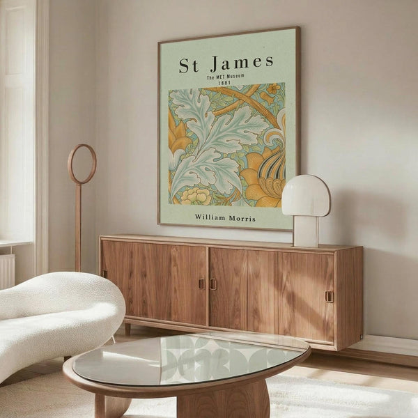 May include: Framed William Morris botanical poster with sage green background and ornate floral pattern in orange and teal tones, displayed above mid-century walnut credenza with sliding doors. Modern white sculptural chair and oval glass coffee table visible in minimalist living room with cream walls and natural lighting.