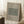 May include: Framed botanical poster leaning against white wall featuring green textured pattern sample labeled "Cotton" and "Eye Bright" with William Morris attribution and dates 1882-1883. Displayed beside wooden block with white coffee cup and saucer, neutral textured rug, and beige throw blanket in soft natural lighting.