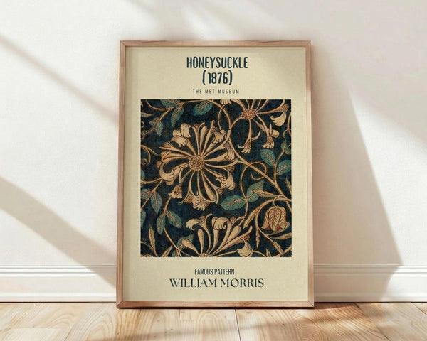 May include: Framed poster with William Morris honeysuckle pattern from 1876 displayed against white wall on wooden floor. Features intricate floral design with large stylized honeysuckle blooms and twisting vines in gold and green tones on dark blue background. Light wooden frame with cream matting. Natural sunlight creates soft shadows across the scene.
