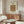 May include: Framed William Morris textile pattern poster with peacock and dragon motifs in coral, green and gold tones displayed above mid-century modern walnut credenza in minimalist living room with cream chair, glass coffee table, and modern lighting