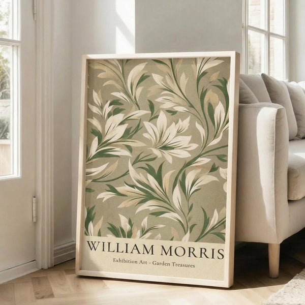 May include: Framed botanical art print leaning against beige couch in bright living room with white walls and large windows. The poster features flowing green and cream leaf patterns in vintage Arts and Crafts style on tan background, displayed in light wood frame on hardwood floor next to neutral sofa.
