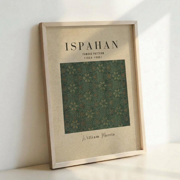 Framed poster featuring William Morris's Ispahan pattern in green and gold tones, displayed in a light wooden frame against a white wall. The design shows an intricate floral and foliage motif typical of Morris's decorative style, with text identifying it as a famous pattern from 1834-1886. The print has a vintage, cream-colored background that complements the ornate botanical design.