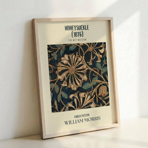 May include: Framed poster print featuring an ornate floral pattern with large stylized honeysuckle flowers and leaves in gold, cream, and teal colors on a dark blue background. The vintage-style botanical design is displayed in a light wood frame with cream matting, leaning against a white wall. Museum-style typography appears above and below the decorative motif.