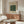 May include: Framed William Morris Ispahan pattern print with green ornate floral design on cream background, displayed above mid-century walnut credenza in minimalist living room with white sculptural chair, glass coffee table, and modern brass floor lamp