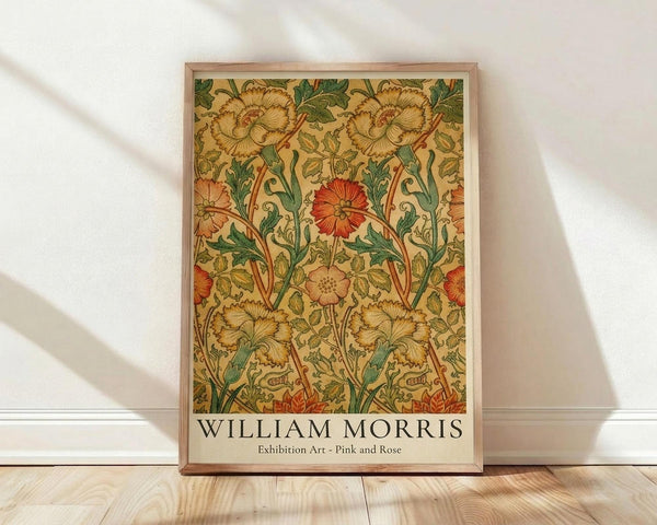 May include: Framed poster with William Morris floral pattern featuring golden yellow carnations, red roses, and green foliage on cream background, displayed against white wall on light wood floor with natural sunlight shadows