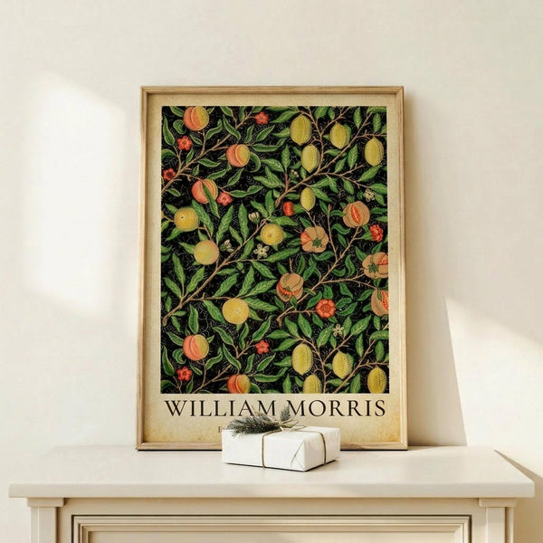 May include: Framed botanical poster with dark background featuring green foliage, orange peaches, yellow lemons, and red berries in decorative pattern. Light wood frame displays on white shelf next to small wrapped gift with twine and evergreen sprig against cream wall.