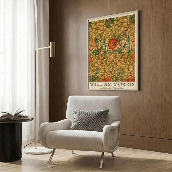 May include: Framed William Morris botanical artwork with yellow, orange, and green floral pattern displayed on wood-paneled wall above modern cream armchair with geometric pillow, brass floor lamp, and dark round side table with open book in contemporary living room setting