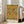 May include: Framed botanical art print leaning against white wall next to beige upholstered chair. The vintage-style poster features an intricate floral pattern with large yellow carnations, red poppies, and green foliage on cream background. Text at bottom reads "WILLIAM MORRIS Exhibition Art - Pink and Rose." Natural sunlight streams through nearby windows onto light wooden floors.