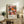 May include: Framed vintage exhibition poster featuring colorful circular patterns in pink, orange, and black with polka dots, displayed on rustic wooden sideboard alongside fern plant, ceramic vase, and books in warm neutral living room setting