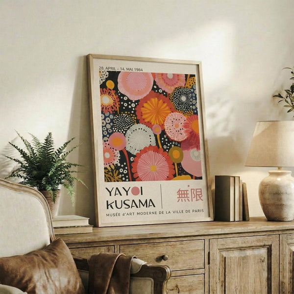 May include: Framed vintage exhibition poster featuring colorful circular patterns in pink, orange, and black with polka dots, displayed on rustic wooden sideboard alongside fern plant, ceramic vase, and books in warm neutral living room setting