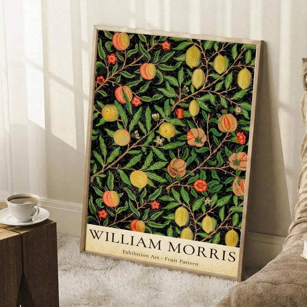 May include: Framed botanical poster with black background featuring colorful fruit and foliage pattern in green, yellow, orange and red tones, leaning against white wall next to white coffee cup on wooden surface and beige fabric.