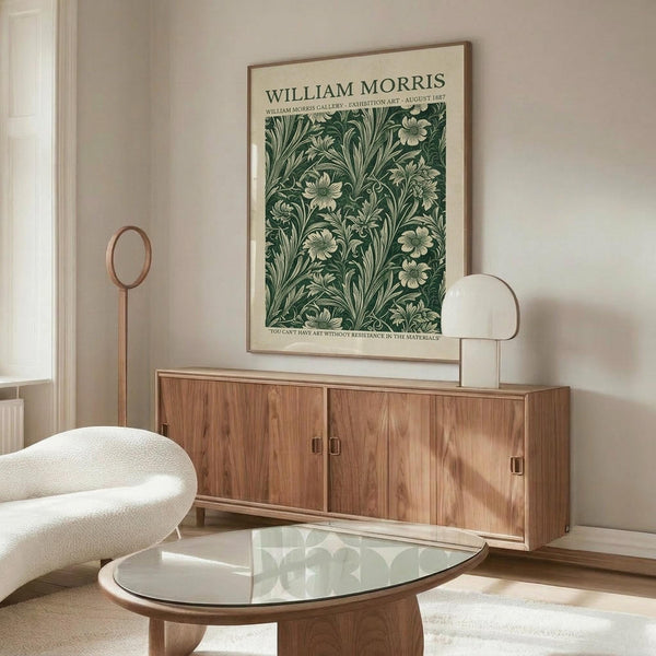 May include: Framed botanical poster with green floral pattern displayed above wooden credenza in modern living room. White curved chair and glass oval coffee table visible. Poster shows intricate leaf and flower design in dark green tones with cream text header. Natural lighting creates shadows across warm wood furniture and neutral walls.