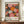 May include: Framed exhibition poster featuring vibrant circular and radial patterns in pink, coral, yellow, and navy blue with white polka dots. The artwork shows overlapping fan-like shapes and dotted designs against a dark background. Text reads "28. APRIL - 14. MAI 1984" at top, "YAYOI KUSAMA" and Japanese characters at bottom, with "MUSEE D'ART MODERNE DE LA VILLE DE PARIS" below. Brown wooden frame displayed on wooden sideboard next to white ceramic vase and books in