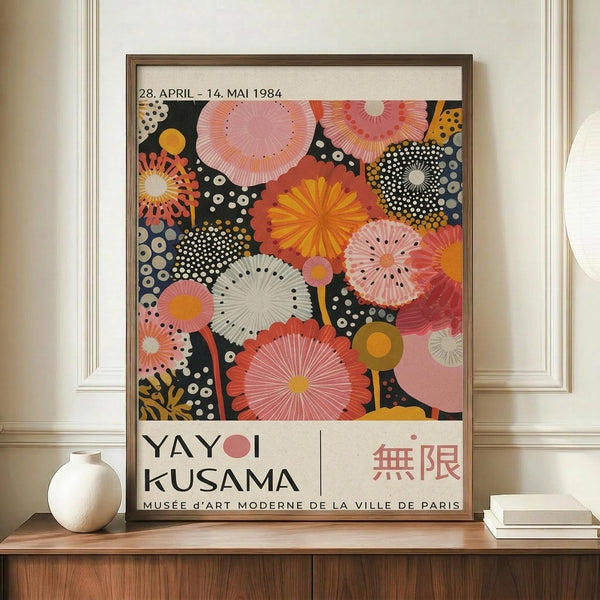 May include: Framed exhibition poster featuring vibrant circular and radial patterns in pink, coral, yellow, and navy blue with white polka dots. The artwork shows overlapping fan-like shapes and dotted designs against a dark background. Text reads "28. APRIL - 14. MAI 1984" at top, "YAYOI KUSAMA" and Japanese characters at bottom, with "MUSEE D'ART MODERNE DE LA VILLE DE PARIS" below. Brown wooden frame displayed on wooden sideboard next to white ceramic vase and books in