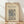 May include: Framed vintage botanical wallpaper design print in cream and blue tones, featuring ornate floral and vine patterns in Arts and Crafts style. Natural wood frame leaning against white wall on light wooden floor with soft shadows from window light.