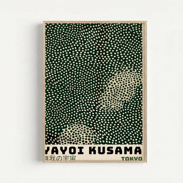 Framed poster featuring dark green background with scattered white polka dots and two large cream-colored oval shapes filled with black dots in a halftone pattern. Text reads "YAYOI KUSAMA" in black letters with Japanese characters and "TOKYO" below. Light wood frame against white wall background.