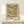 May include: Framed botanical poster featuring William Morris's Trellis pattern with blue birds perched among orange roses and green foliage on a cream background with geometric grid lines. Light wood frame displayed on white wooden furniture beside a small wrapped gift with twine and evergreen sprig against neutral wall.
