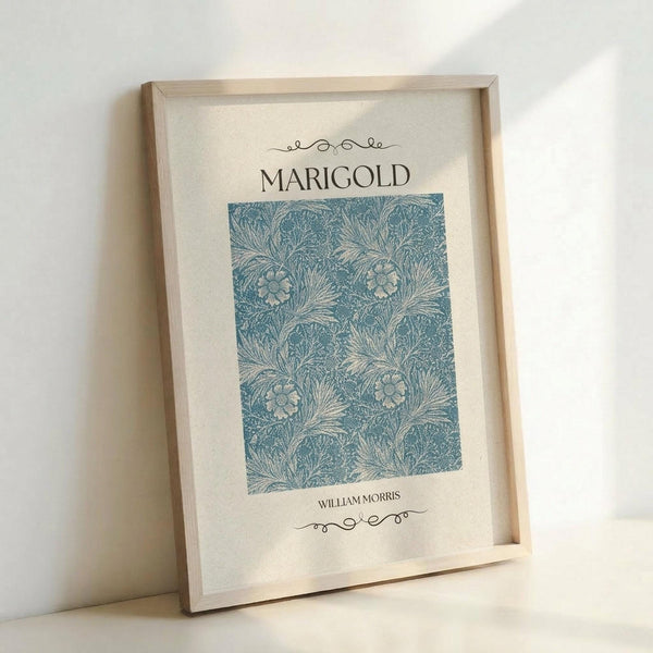 May include: Framed botanical art print featuring William Morris's Marigold pattern in blue-green tones with decorative flowers and flowing foliage design, displayed in light wood frame against white wall corner, casting soft shadows