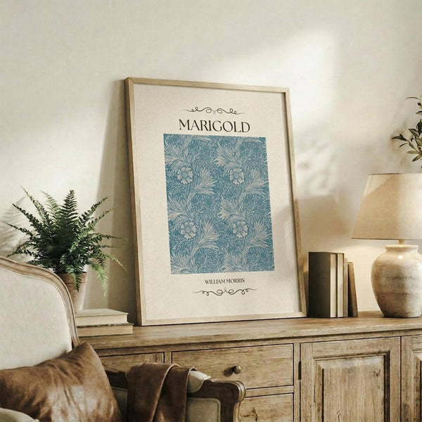 May include: Framed botanical art print with blue floral pattern displayed on rustic wooden sideboard alongside fern plant, books, and ceramic vase in warm neutral living room setting with beige upholstered chair