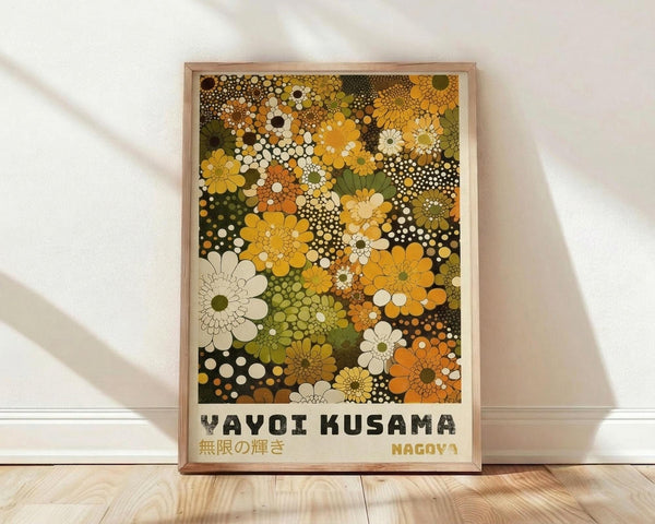 May include: Framed art print featuring colorful floral dot pattern in yellows, oranges, greens, and whites on cream background, displayed against white textured wall on light wood floor. Print shows dense arrangement of stylized flowers and polka dots in warm autumn tones with "YAYOI KUSAMA" and Japanese text at bottom. Natural wood frame with light finish complements the organic botanical design.