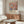 May include: Colorful floral art poster with overlapping circular flower patterns in pink, orange, blue, and green tones, displayed in wooden frame above mid-century modern walnut credenza. Modern living room setting features white curved chair, glass oval coffee table, floor lamp, and neutral walls with natural lighting from curtained window.