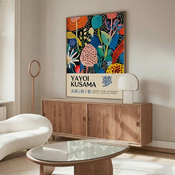 May include: Colorful abstract floral poster featuring vibrant botanical shapes in blues, oranges, pinks and yellows with polka dot patterns, displayed in thin frame on wooden sideboard beside white sculptural lamp and round mirror in modern living room with cream chair and glass coffee table.