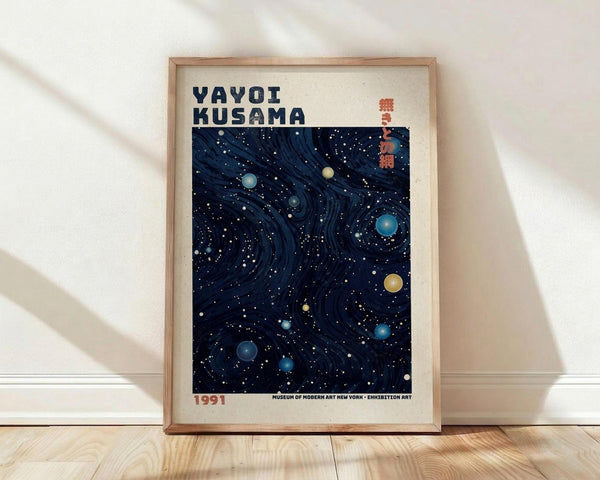 May include: Framed poster with cream matting and light wood frame leaning against white wall on wooden floor. Features dark blue cosmic design with swirling patterns, scattered circular dots in blue, yellow and white representing stars and planets. Text reads "YAYOI KUSAMA" at top with Japanese characters and "1991 MUSEUM OF MODERN ART NEW YORK EXHIBITION ART" at bottom.
