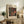 May include: Framed vintage exhibition poster featuring bold polka dot pattern in black, red, and cream colors displayed on rustic wooden sideboard next to fern plant, books, and ceramic vase in warm-toned living room setting