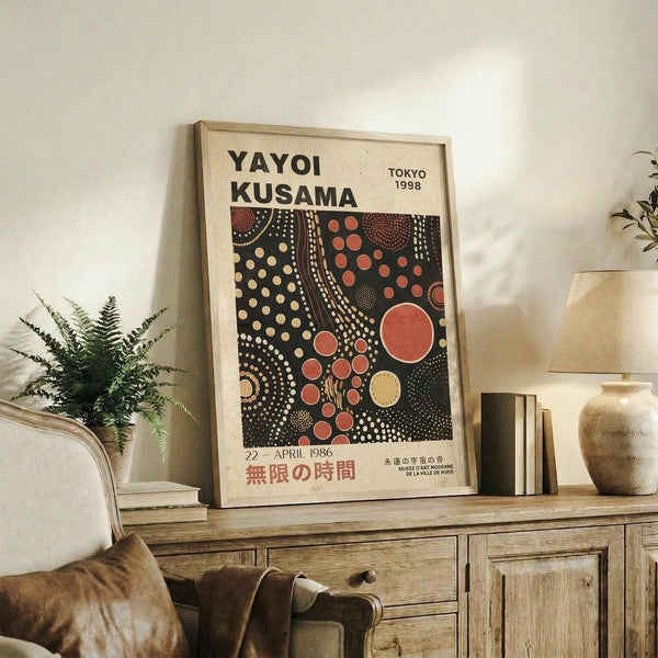May include: Framed vintage exhibition poster featuring bold polka dot pattern in black, red, and cream colors displayed on rustic wooden sideboard next to fern plant, books, and ceramic vase in warm-toned living room setting