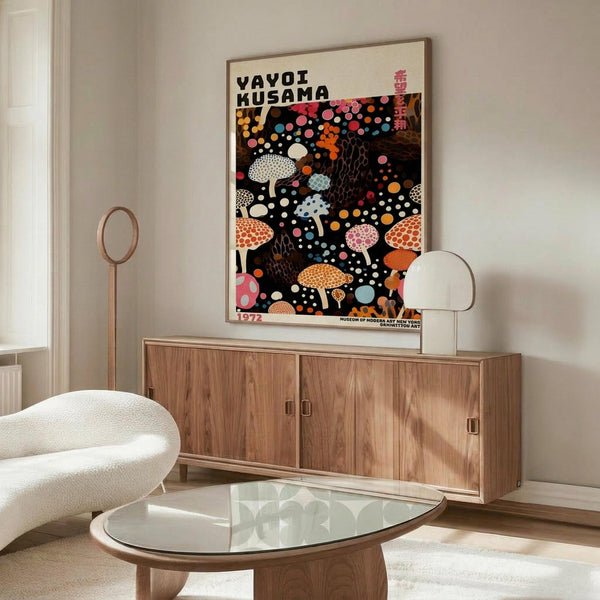 May include: Colorful Yayoi Kusama exhibition poster featuring whimsical mushrooms and polka dots on black background, displayed above mid-century modern walnut credenza in minimalist living room with cream chair, glass coffee table, and neutral walls