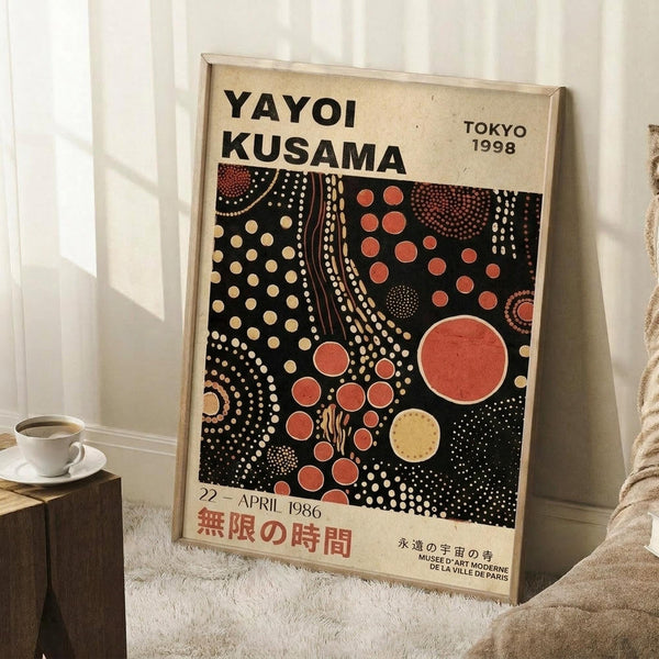 May include: Framed exhibition poster featuring Yayoi Kusama's distinctive polka dot artwork in black background with red, orange, and cream colored circles and flowing dotted patterns. Text shows "YAYOI KUSAMA," "TOKYO 1998," and "22-APRIL 1986" with Japanese characters. Poster leans against white wall corner next to coffee cup on wooden block and beige fabric, displaying vintage museum exhibition design with cream matting and natural wood frame.