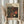 May include: Person in beige clothing holding framed poster with abstract polka dot pattern in black, red, orange and cream colors, alongside dried pampas grass stems against white curtained background. Frame appears light wood with cream matting, poster features Japanese text and museum information.