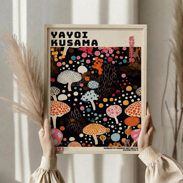 May include: Person in beige ruffled sleeves holding framed art poster against white curtained window, with dried wheat stalks visible. The vintage-style poster features colorful polka-dotted mushrooms and abstract shapes on black background, displayed in light wood frame. Museum exhibition artwork with bold typography and scattered circular patterns in orange, pink, white, and blue tones.