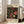 May include: Framed exhibition poster featuring Yayoi Kusama's signature polka dot artwork in black, red, orange and cream colors, displayed on wooden floor next to beige armchair in bright room with white walls and windows. The vintage-style poster shows circular dot patterns and museum exhibition text in both English and Japanese characters.