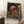 May include: Framed poster artwork featuring vibrant psychedelic mushrooms in red, orange, yellow, and teal colors against black starry background, displayed in light wood frame leaning against white wall corner. Coffee cup on wooden block and cream knit throw visible nearby on light carpet. Japanese text appears at bottom of colorful botanical illustration.