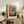 May include: Colorful fish artwork in light wood frame displayed on rustic wooden sideboard next to fern plant, books, and ceramic vase. The vibrant poster features a stylized fish with large black eye surrounded by multicolored dots in rainbow hues against blue background. Japanese text appears at top and bottom of print in simple modern font.