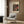 May include: Cream-colored vintage exhibition poster featuring red and yellow polka dot pattern on dark background, displayed in modern room setting with beige upholstered armchair, geometric throw pillow, brass floor lamp, and wood-paneled wall. Japanese text visible at bottom of framed artwork.