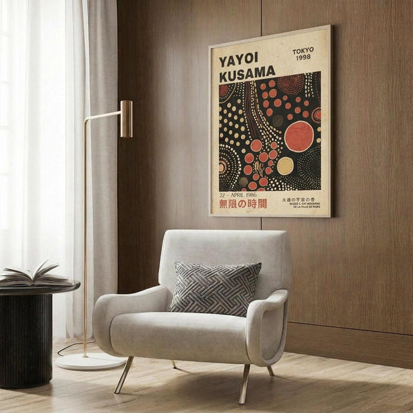 May include: Cream-colored vintage exhibition poster featuring red and yellow polka dot pattern on dark background, displayed in modern room setting with beige upholstered armchair, geometric throw pillow, brass floor lamp, and wood-paneled wall. Japanese text visible at bottom of framed artwork.