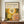 May include: Framed poster with abstract circular dot patterns in yellow, orange, and green tones displayed on wooden sideboard next to white ceramic vase and books. The artwork features large radiating circles made of dots in warm colors against dark background, shown in brown frame against cream walls with white molding.